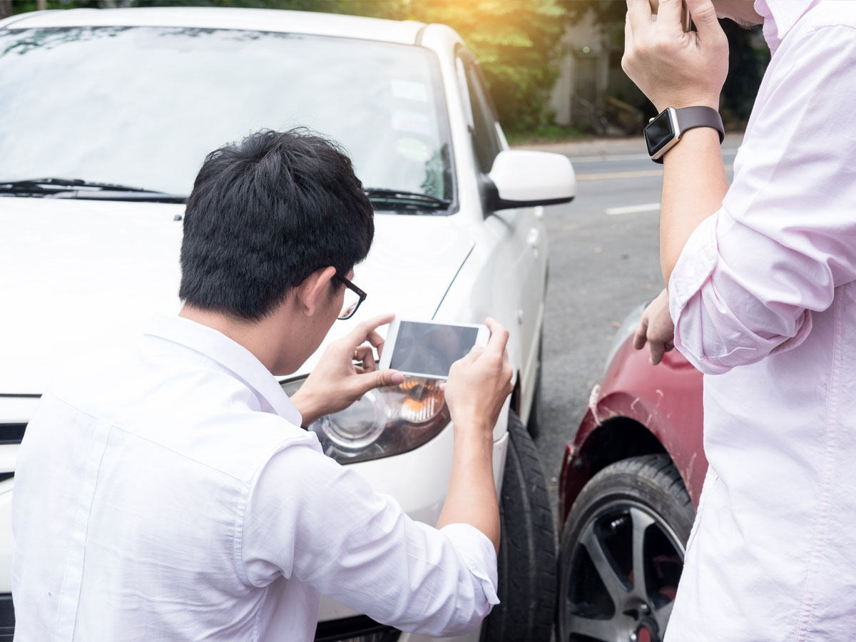 Male Driver take pictures of accident-damaged vehicle with a holding smartphone After Traffic Collision proof of insurance claim.